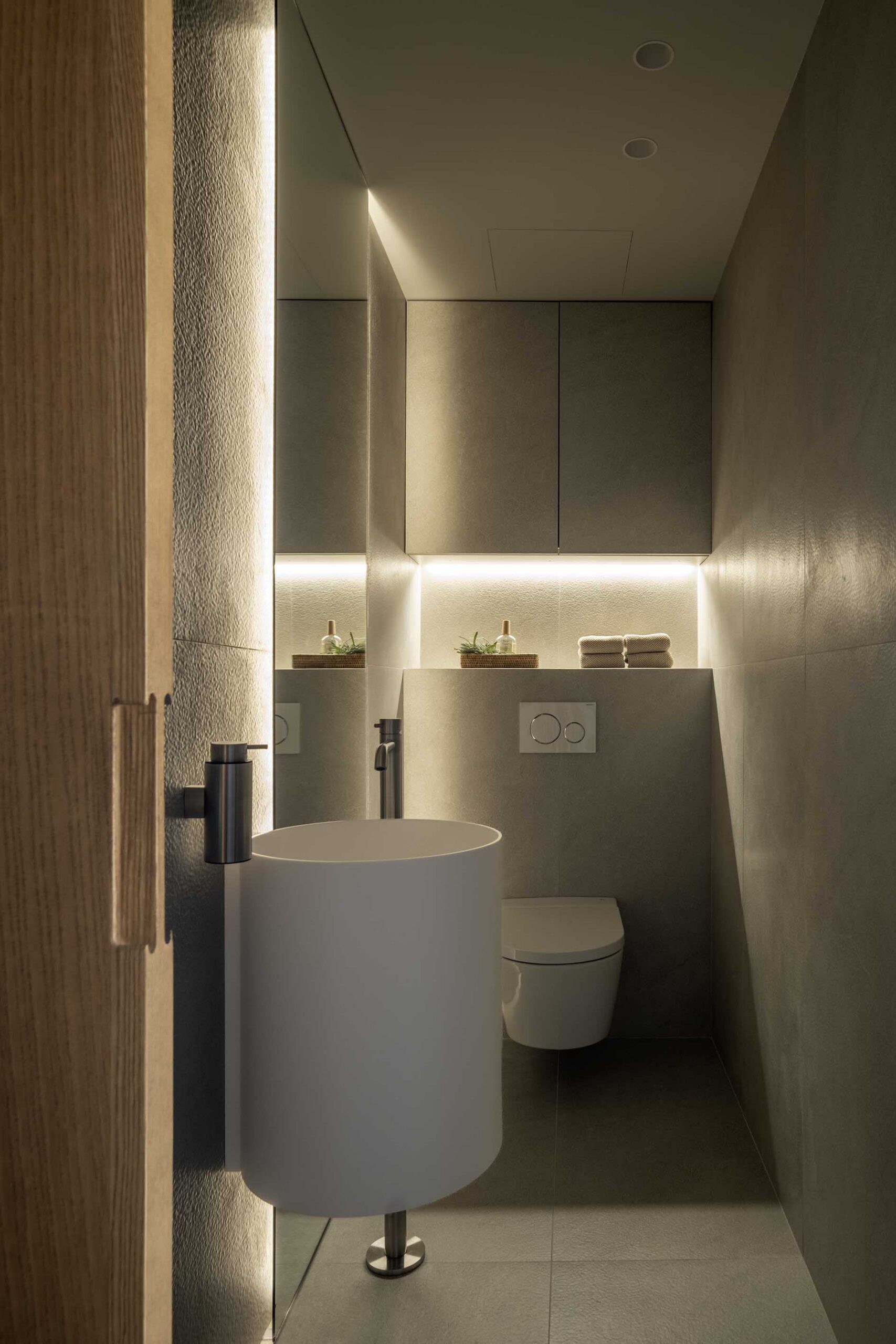 Guest WC with white cylindrical basin, grey cladding and integrated indirect lighting