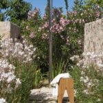 Detalle de la ducha exterior metálica con taburete de madera y toalla entre flores