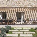 Porche con comedor y zona de estar bajo pérgola, con sombras sobre el muro de piedra