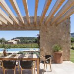 Vigas de madera de la pérgola sobre mesa de comedor, con piscina y viñedo al fondo