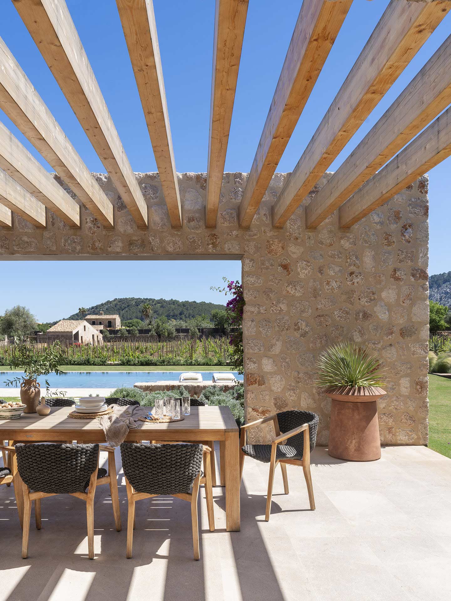 Vigas de madera de la pérgola sobre mesa de comedor, con piscina y viñedo al fondo