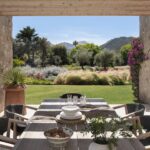 Mesa de comedor exterior bajo pérgola de madera con vistas al jardín y a la montaña