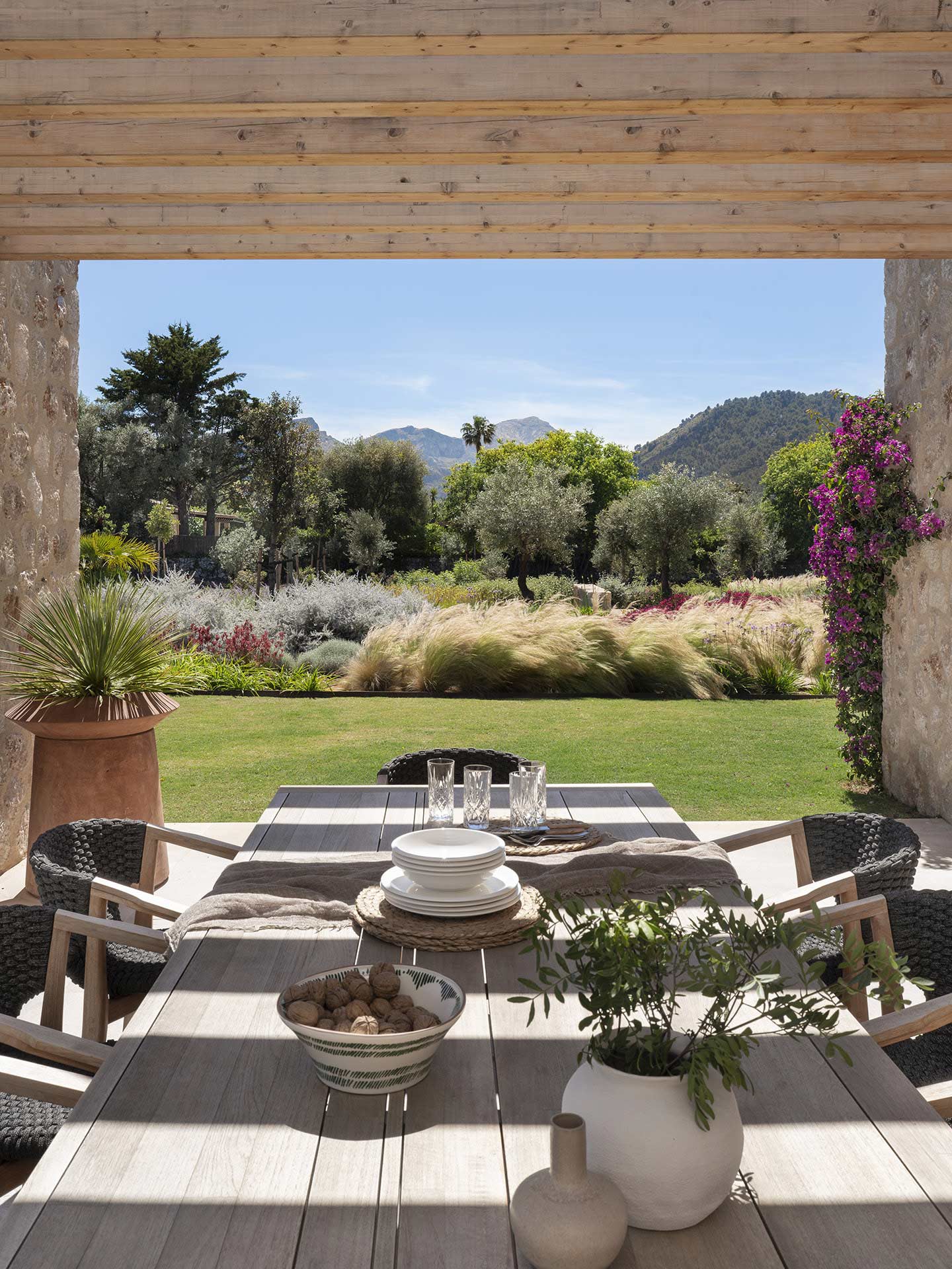 Mesa de comedor exterior bajo pérgola de madera con vistas al jardín y a la montaña