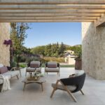 Zona de estar exterior con sofá y butacas de fibra bajo pérgola, entre muros de piedra