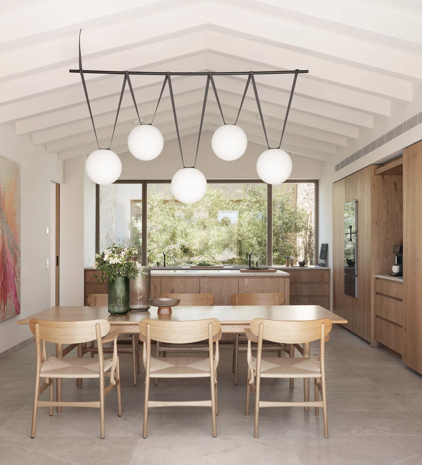 Comedor y cocina con armarios de madera, lámpara de esferas y ventanal hacia el patio