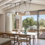 Comedor con mesa y sillas de madera clara bajo lámpara de esferas blancas, abierto a la terraza
