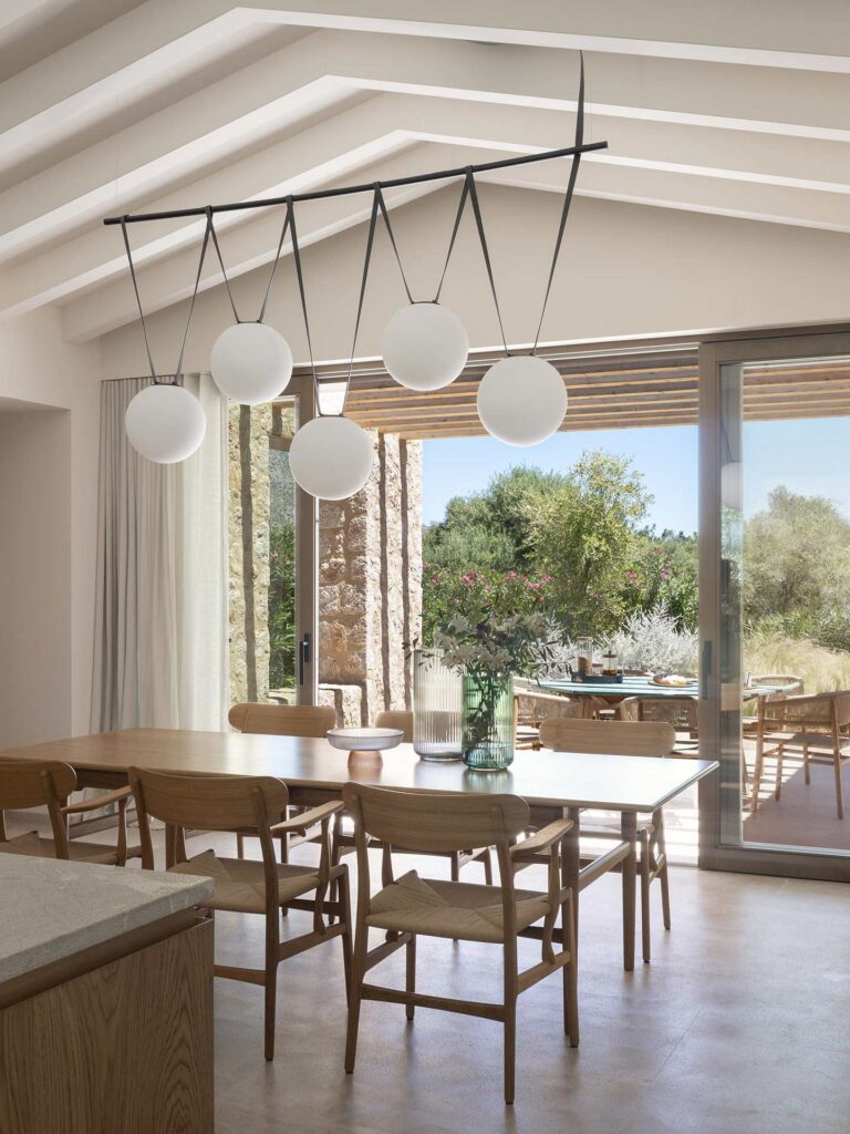 Comedor con mesa y sillas de madera clara bajo lámpara de esferas blancas, abierto a la terraza