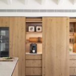 Armarios de madera con puerta corredera abierta que deja ver cafetera y estantes iluminados