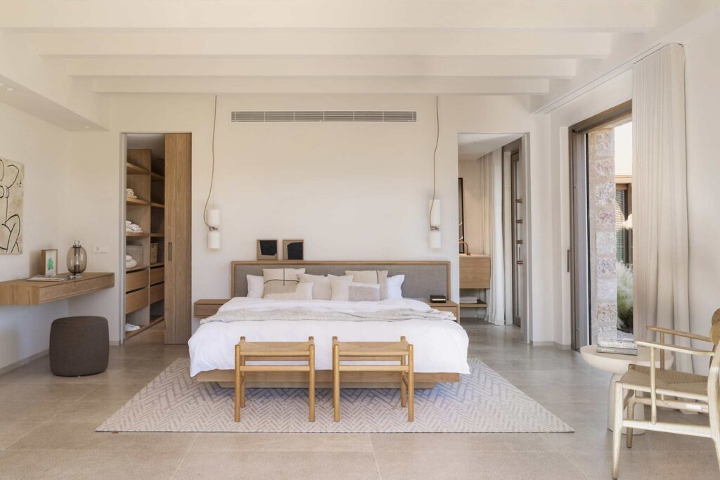 Dormitorio con cama de madera y cabecero tapizado, vestidor abierto y suelo de piedra clara