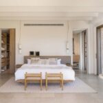 Dormitorio con cama de madera y cabecero tapizado, vestidor abierto y suelo de piedra clara