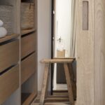Detalle del vestidor con cajones de madera, cestas de fibra, taburete antiguo y puerta corredera