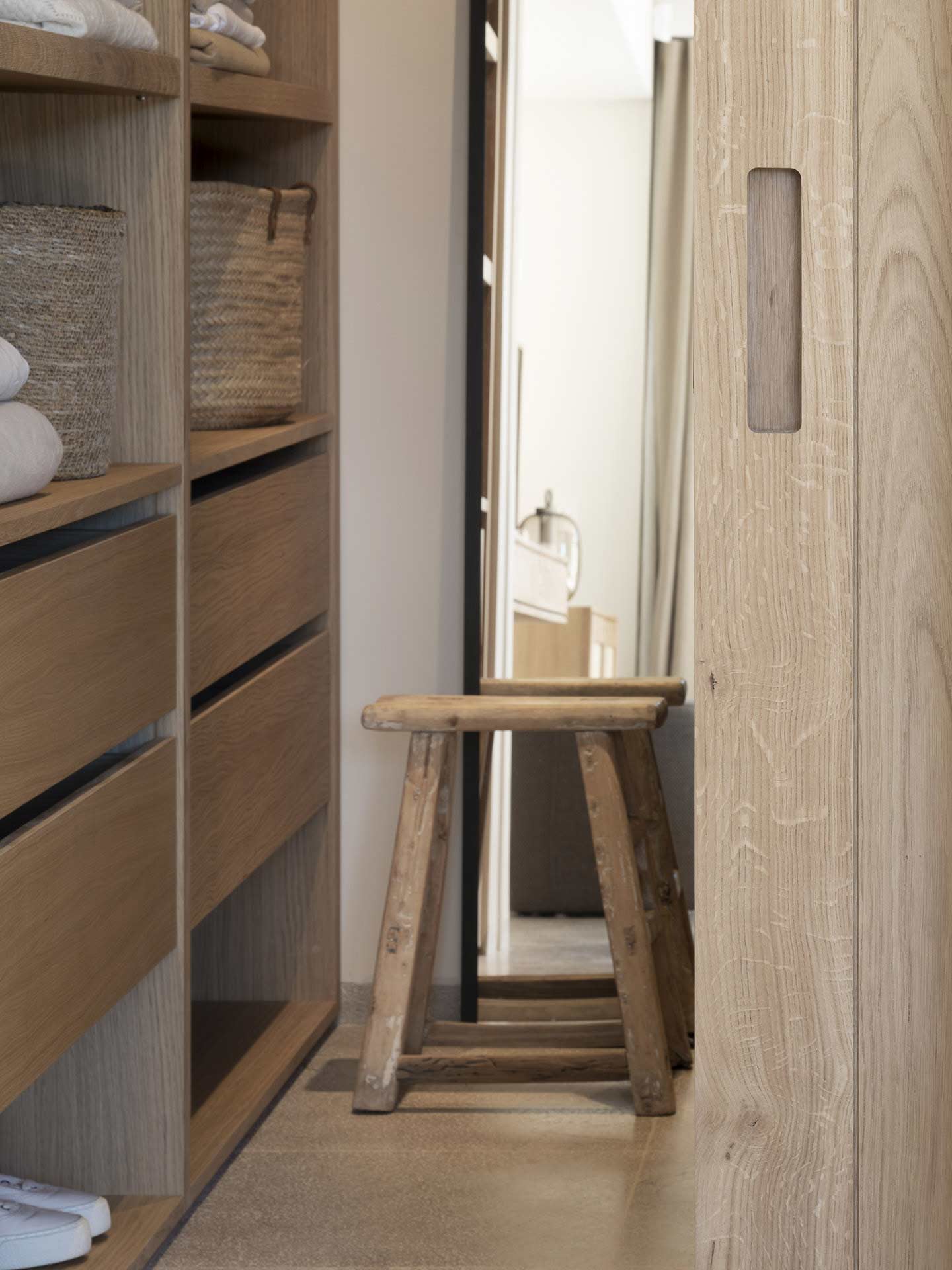 Detalle del vestidor con cajones de madera, cestas de fibra, taburete antiguo y puerta corredera