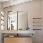 Baño con doble lavabo de piedra, espejos de marco negro, toalleros de cobre y mueble de madera