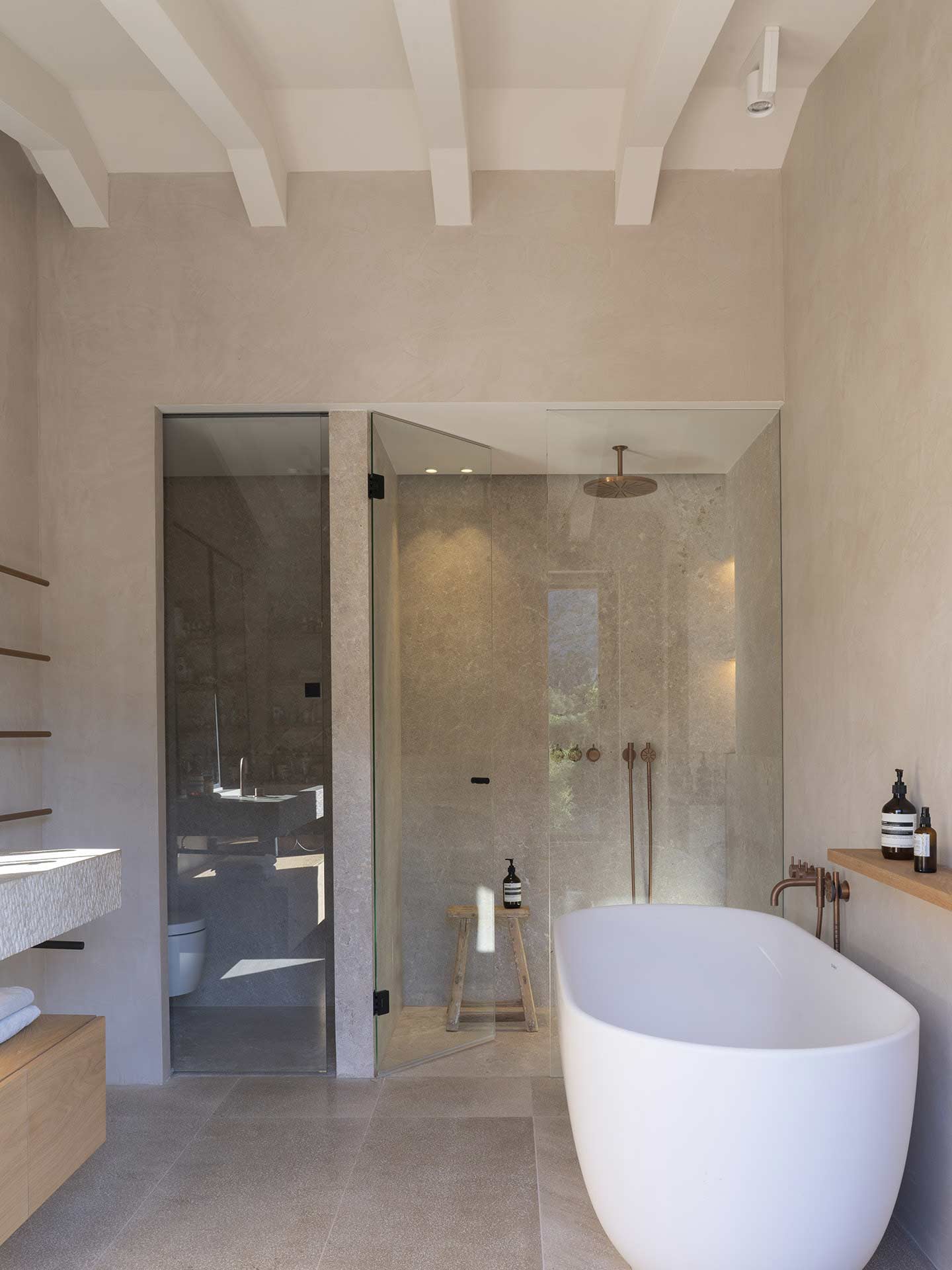 Baño con bañera exenta blanca, ducha acristalada revestida de piedra y grifería de cobre