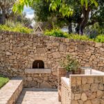 Rincón de cocina exterior con horno de leña empotrado en un muro de piedra seca