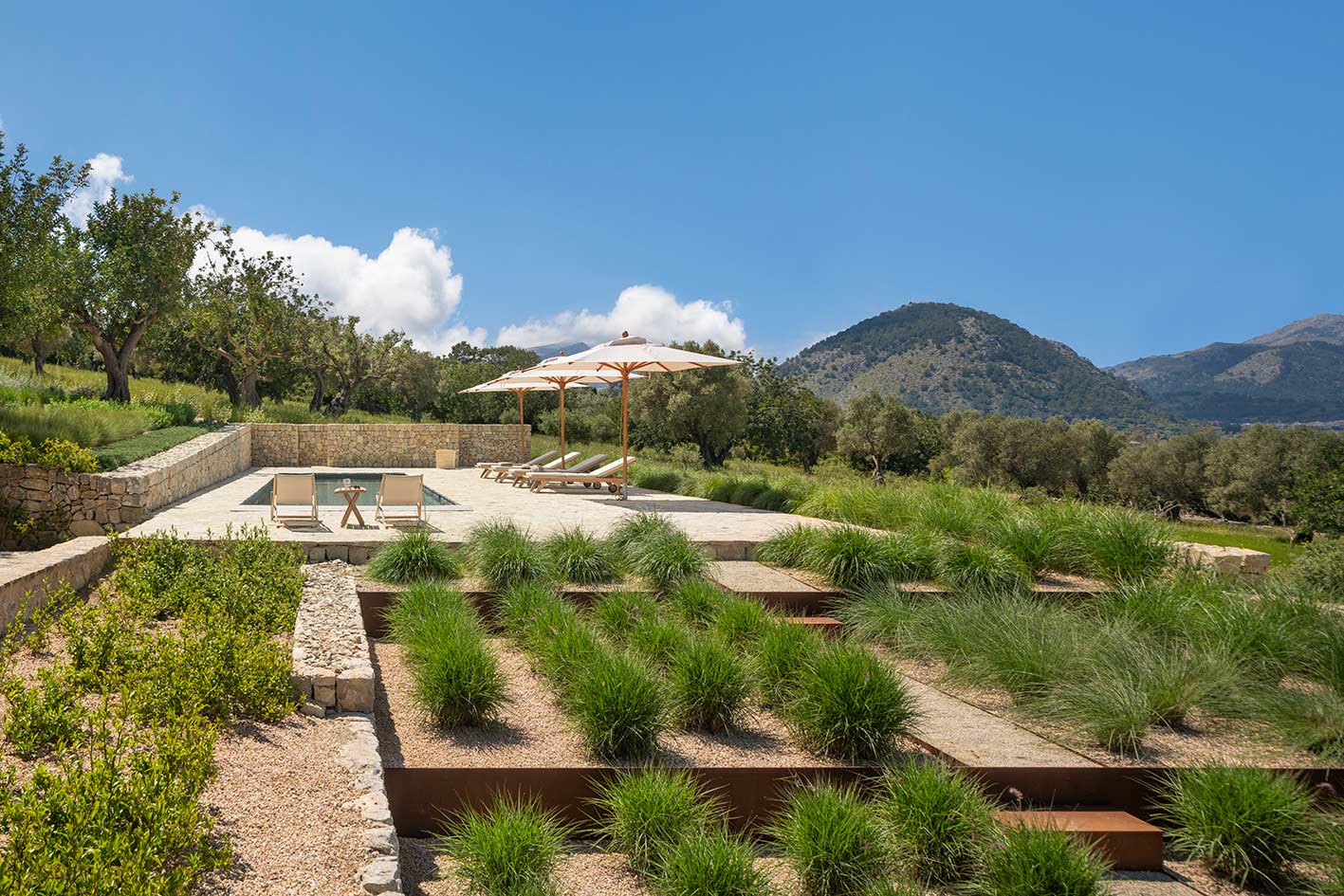 Jardín en bancales con gramíneas y bordes de acero corten, con la piscina y las montañas al fondo