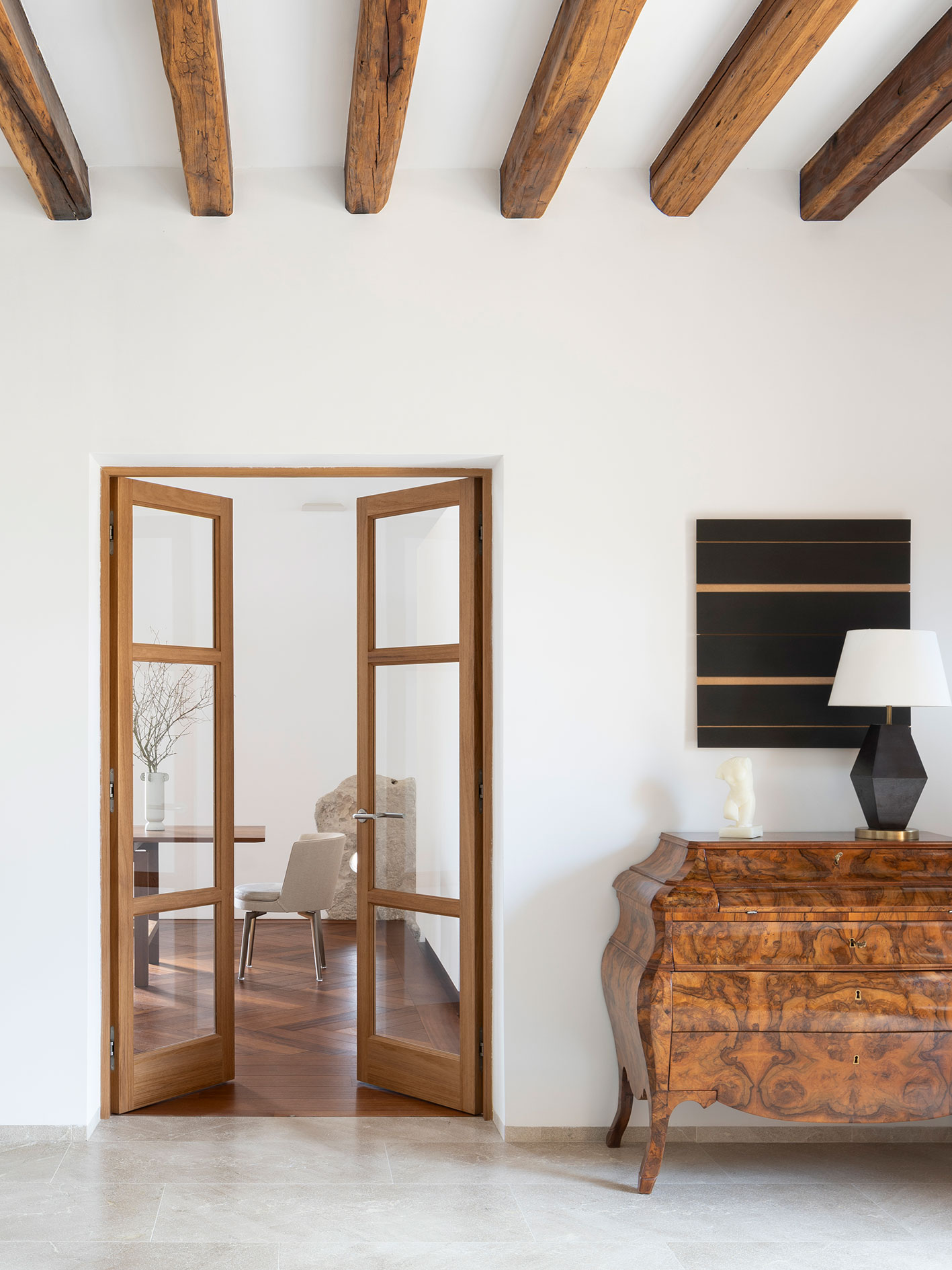 Detalle de vigas de madera vistas, puertas acristaladas de madera y cómoda antigua con lámpara