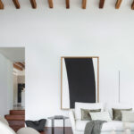 Detalle del salón con sofá blanco, cuadro grande de marco de madera, mesa auxiliar negra y vigas
