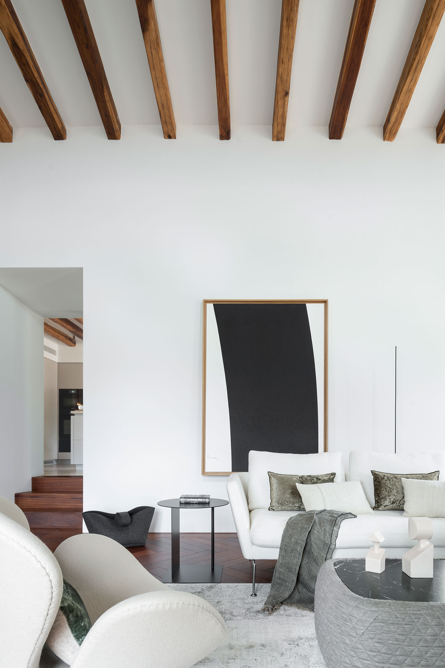 Detalle del salón con sofá blanco, cuadro grande de marco de madera, mesa auxiliar negra y vigas