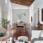 Comedor de techo inclinado con vigas de madera, mesa larga, sillas tapizadas y suelo en espiga