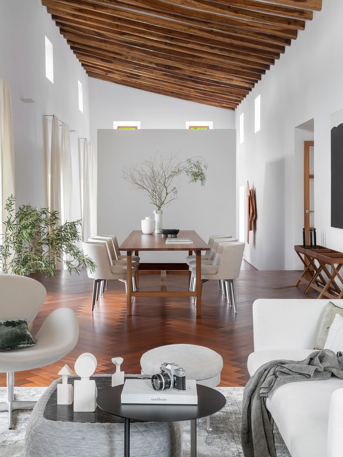 Comedor de techo inclinado con vigas de madera, mesa larga, sillas tapizadas y suelo en espiga