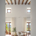 Sala de doble altura con ventanas altas, cortinas claras y puertas acristaladas con vistas a la montaña