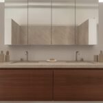 Baño con doble lavabo de piedra, mueble volado de madera oscura y armario de espejos con grifería metálica
