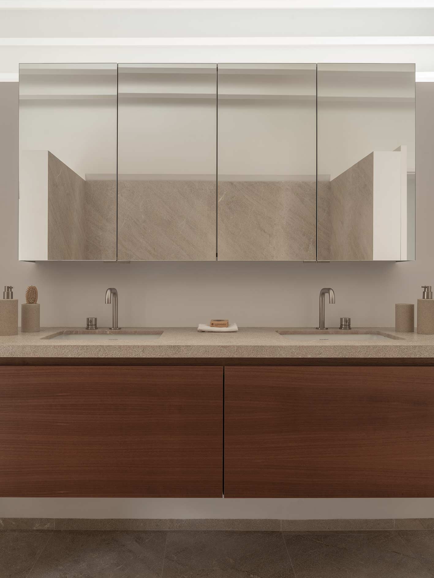 Baño con doble lavabo de piedra, mueble volado de madera oscura y armario de espejos con grifería metálica