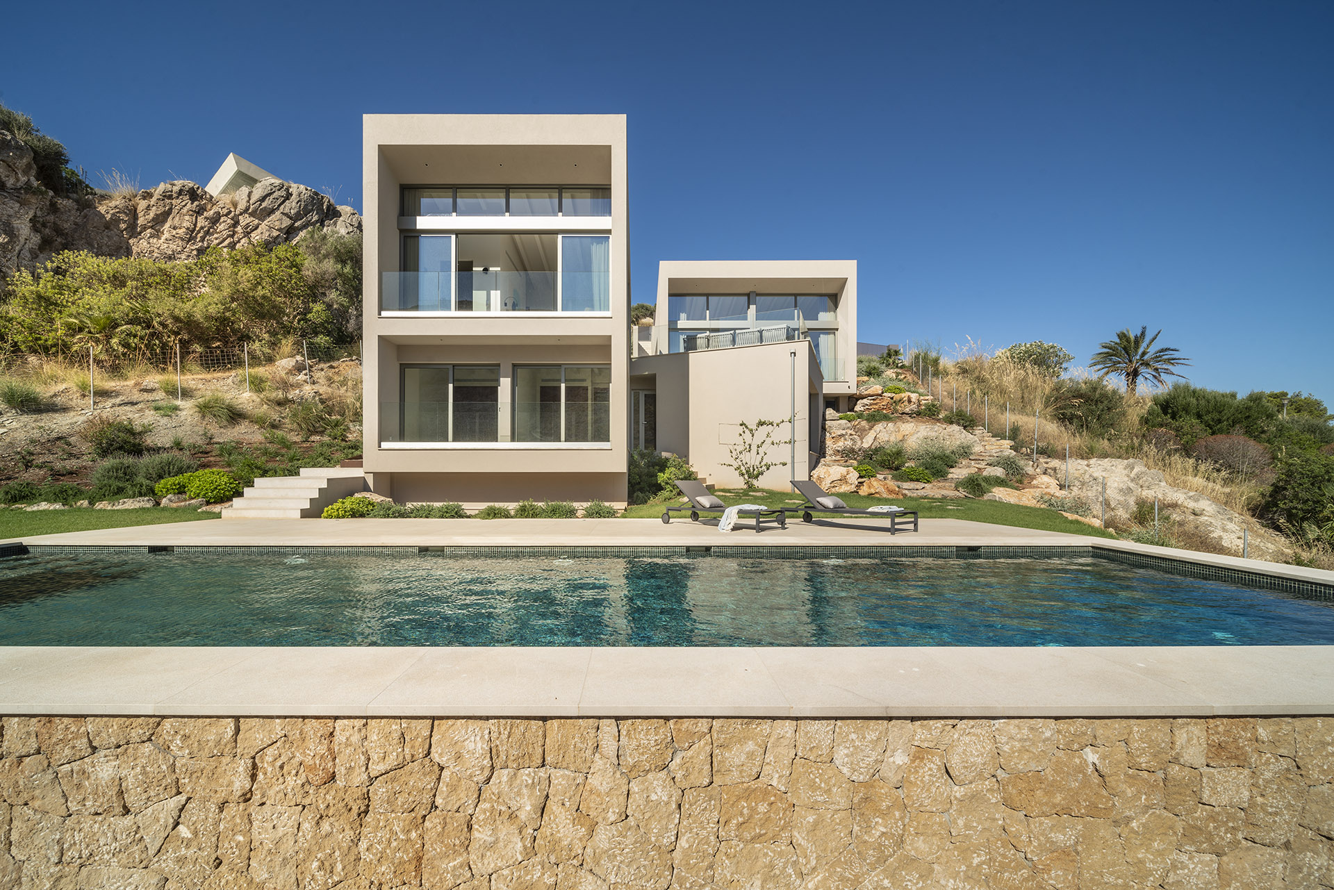 Villa LF91CG01 con fachada de volúmenes beige, piscina y muro de piedra natural en primer plano