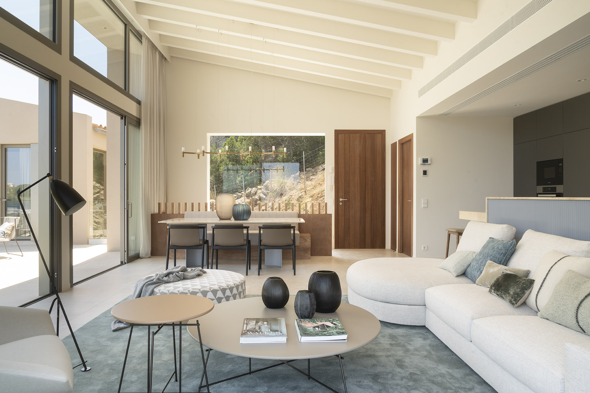 Offener Wohn- und Essbereich mit weißen Balken, geschwungenem Sofa, Esstisch und Küche im Hintergrund