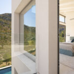 Glasbalkon und Schlafzimmer mit blauem Bettkopfteil, Blick auf den Hang und den Pool