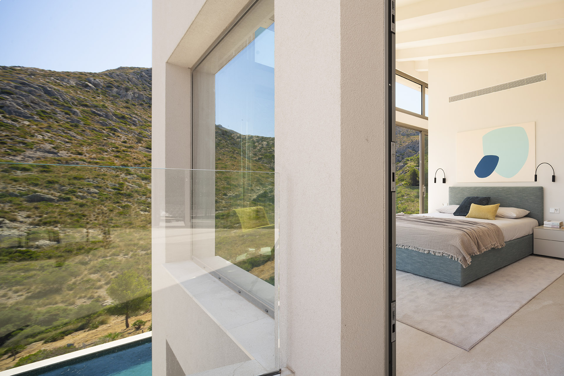 Glasbalkon und Schlafzimmer mit blauem Bettkopfteil, Blick auf den Hang und den Pool