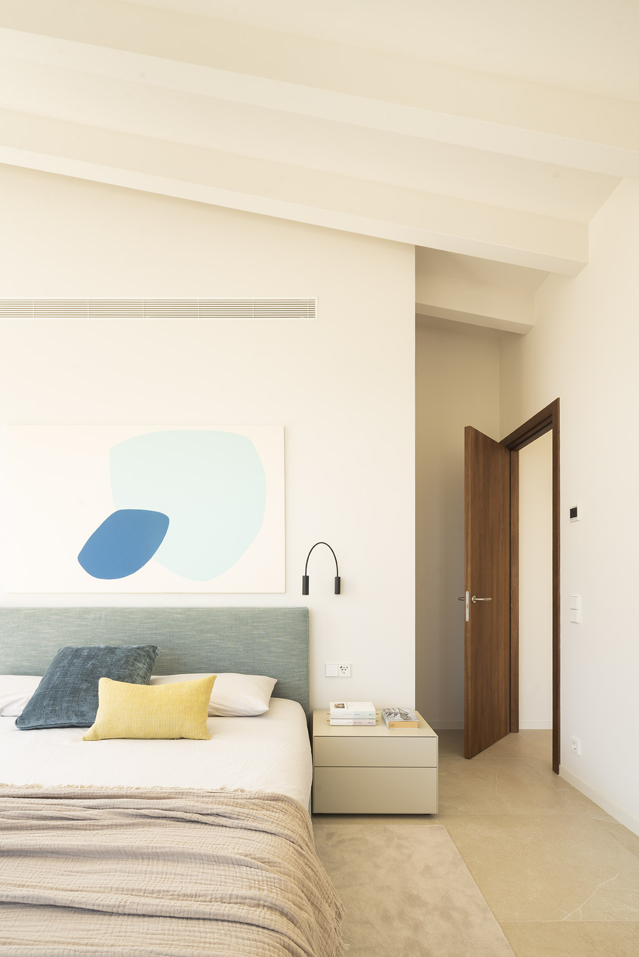 Schlafzimmer mit blaugrünem Kopfteil, abstraktem Gemälde, Decke mit weißen Balken und Holztür