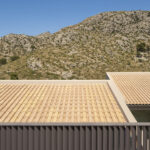 Cubiertas de teja cerámica naranja con barandilla de lamas y montaña rocosa al fondo