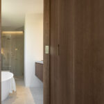 Holzschiebetüren, die den Blick auf ein Bad mit weißer freistehender Badewanne und verglaster Dusche freigeben