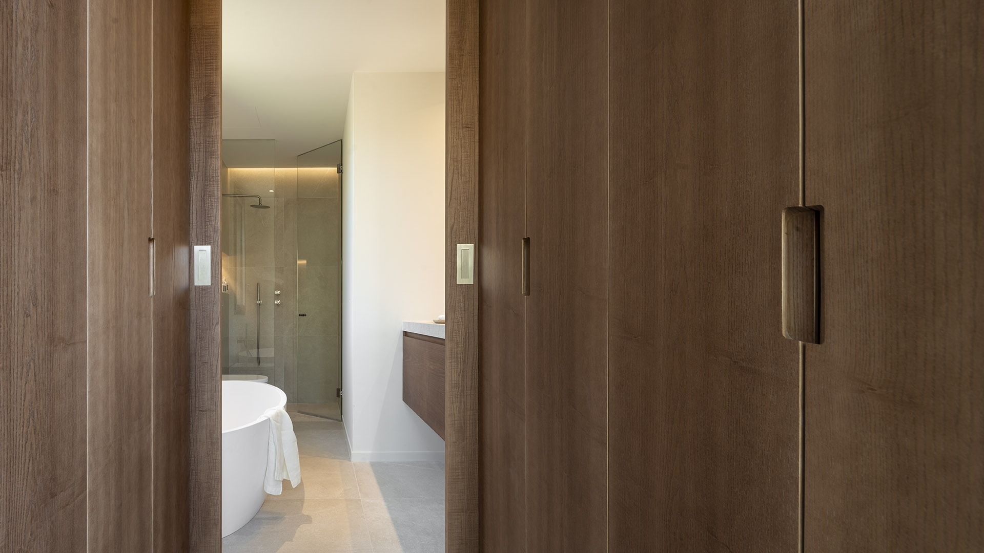 Holzschiebetüren, die den Blick auf ein Bad mit weißer freistehender Badewanne und verglaster Dusche freigeben