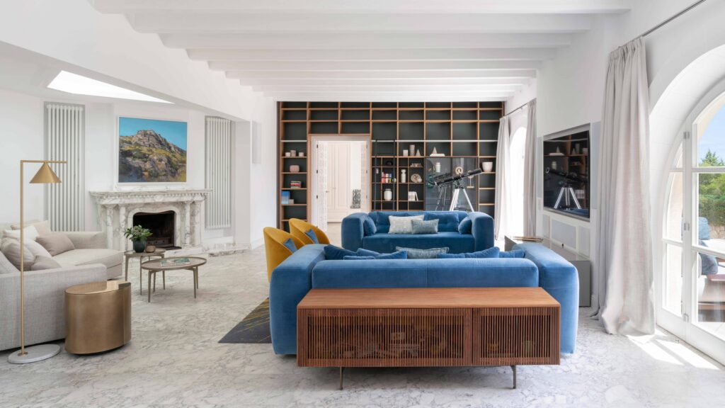 Salón con sofás azules de terciopelo, chimenea de mármol y librería de madera al fondo