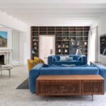 Salón con sofás azules de terciopelo, chimenea de mármol y librería de madera al fondo