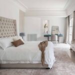 Dormitorio principal con cabecero capitoné beige, escritorio azul, alfombra rosada y luz natural
