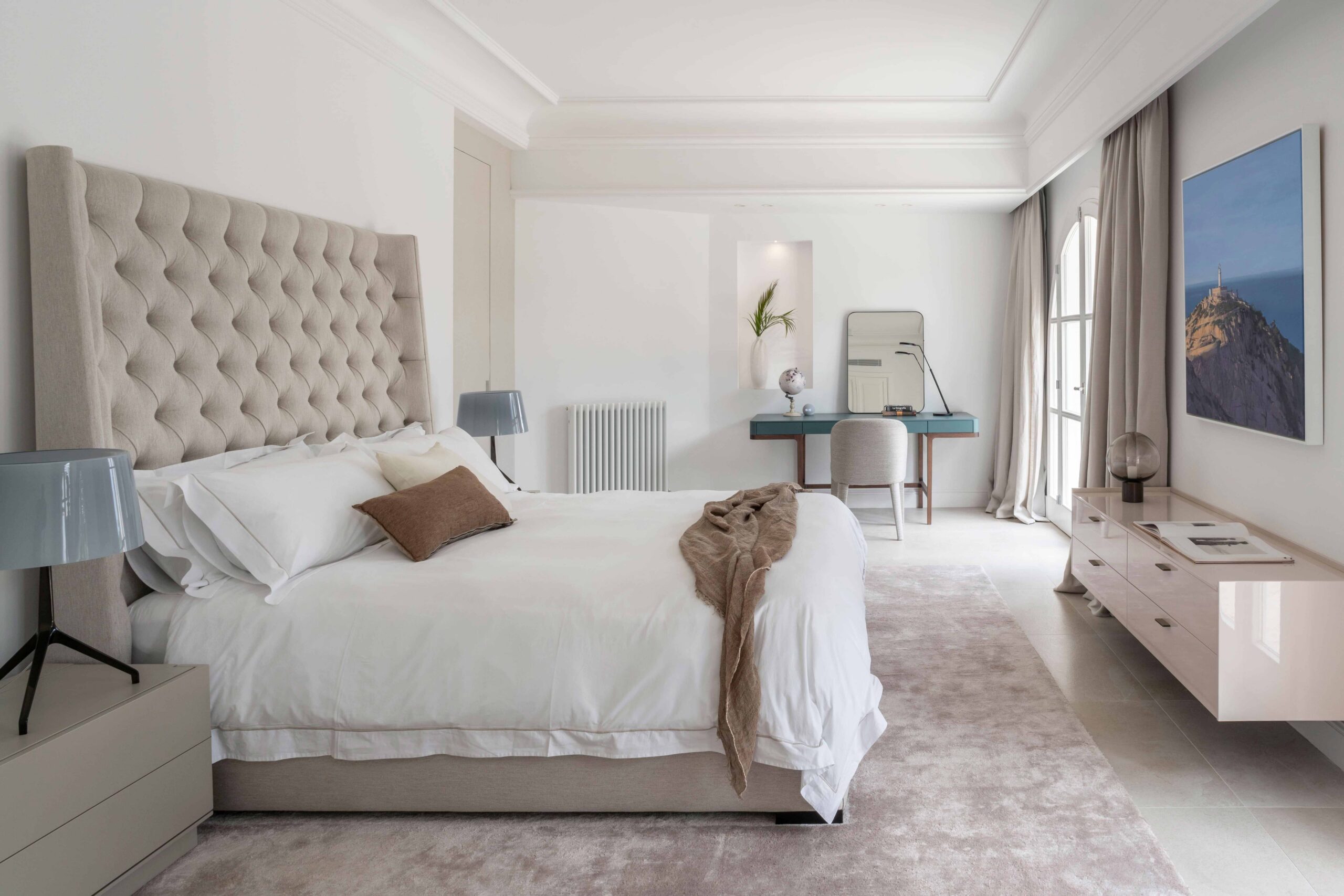 Dormitorio principal con cabecero capitoné beige, escritorio azul, alfombra rosada y luz natural