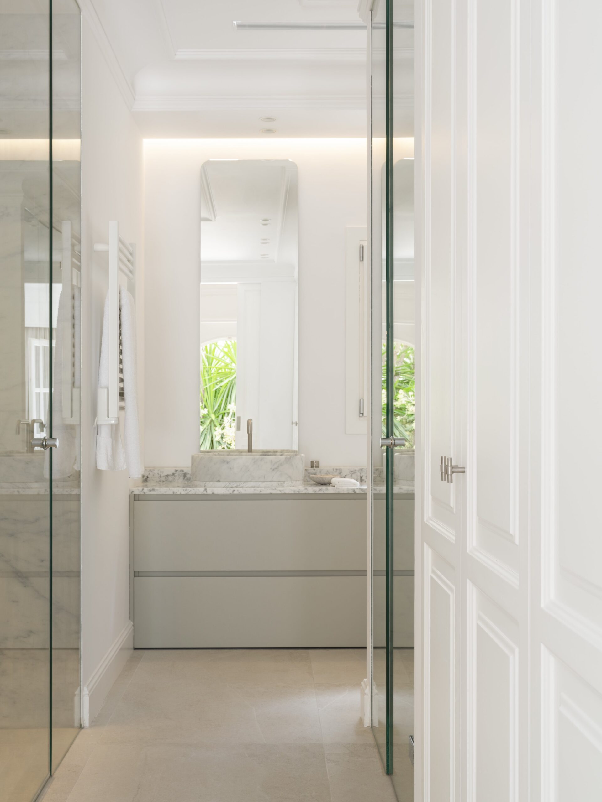 Baño con lavabo de mármol sobre mueble gris claro, espejo alto y mampara de cristal