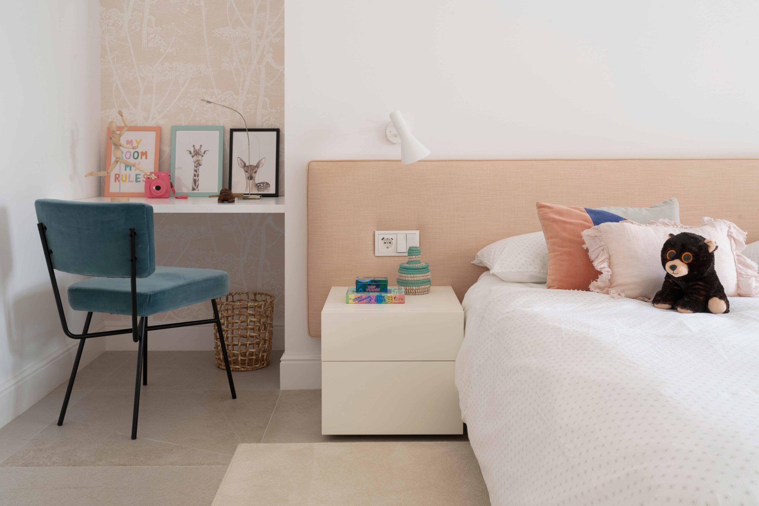 Dormitorio infantil con cabecero color melocotón, escritorio empotrado, silla azul de terciopelo y osito de peluche