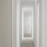 Pasillo blanco con suelo gris y puerta en arco con relieve de rombos al fondo