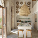 Cocina de techos altos con isla blanca, taburetes de madera, lámpara de esparto y luz natural