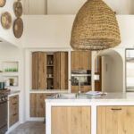 Isla de cocina con fregadero, frentes de madera clara, armario plegable y gran lámpara de esparto