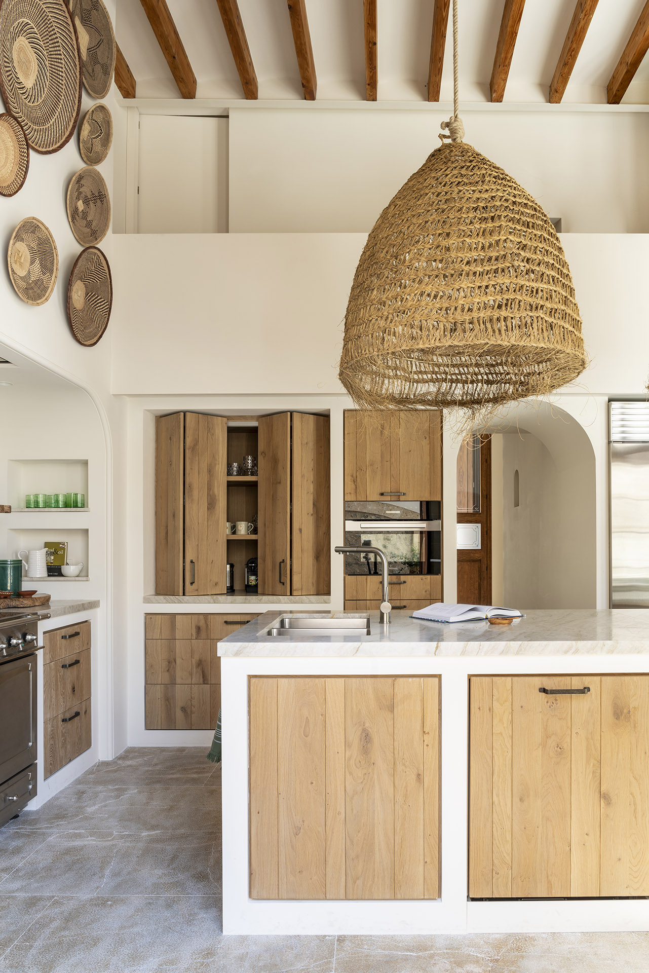 Isla de cocina con fregadero, frentes de madera clara, armario plegable y gran lámpara de esparto