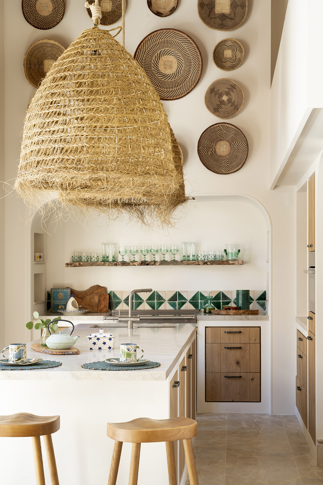 Detalle de cocina con lámpara de esparto, cestas en la pared, estante de vasos y azulejos verdes