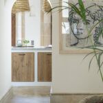 Pasillo con arco blanco que enmarca la cocina, armarios de madera, cuadro con rostro y palmera