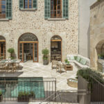 Can Patro, patio central con piscina, fachada de piedra, contraventanas verdes y comedor exterior