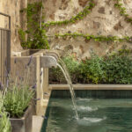 Detalle de la fuente de piedra con chorro de agua cayendo a la piscina, enredadera y lavanda